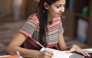 An image of a young woman taking notes and working on her laptop.